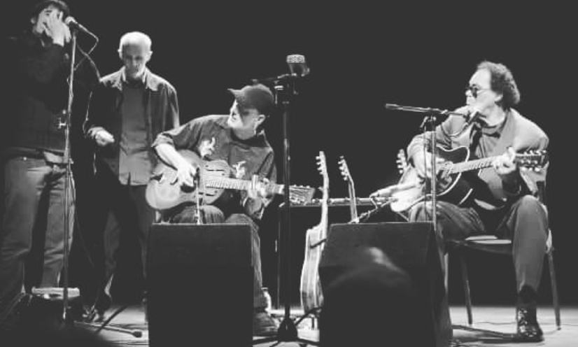 Marco Farris on harmonica with three acoustic guitarists on a theatre stage