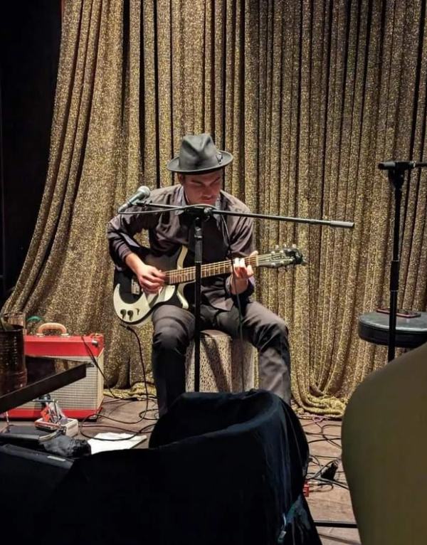 Marco Farris seated on stage with an electric guitar