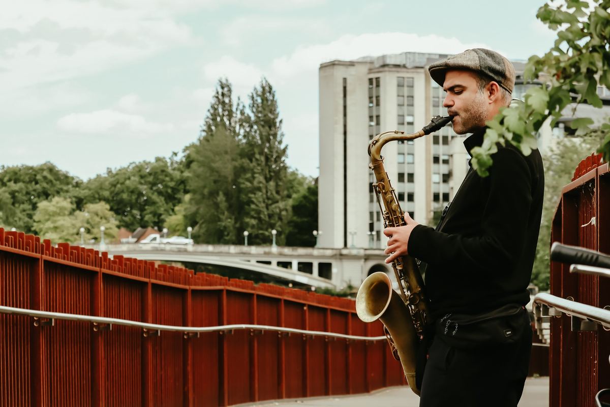 Marco Farris playing tenor saxophone on a bridge by the river