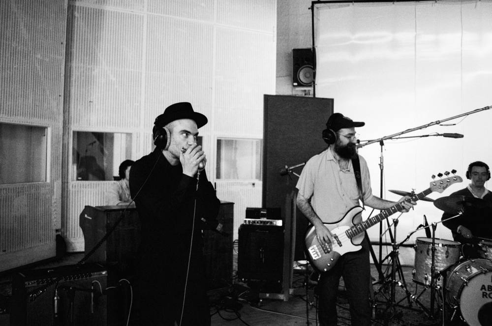 Marco Farris on harmonica with headphones during a studio session, bass player beside him