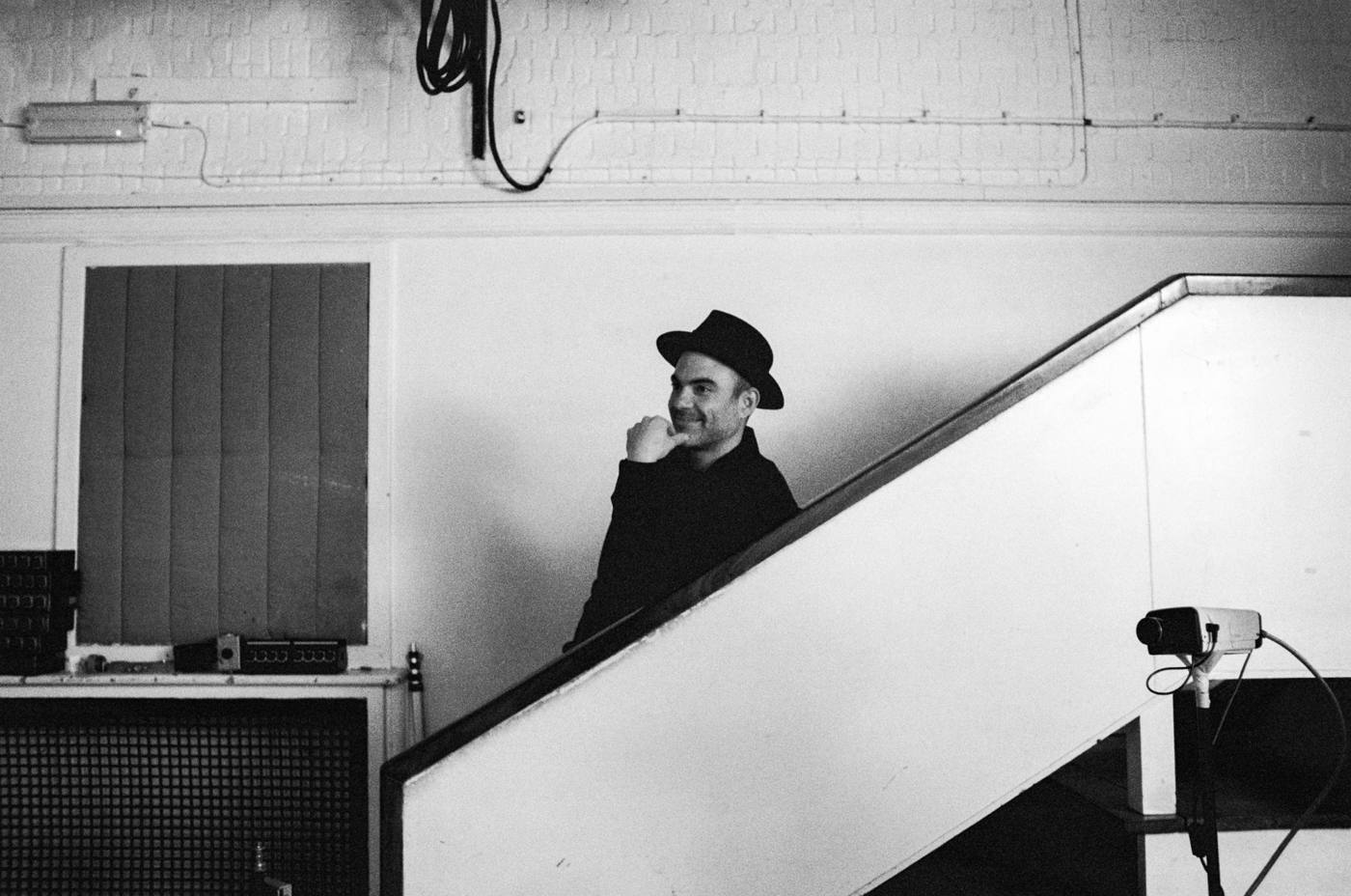 Marco Farris in a hat, smiling on a studio staircase