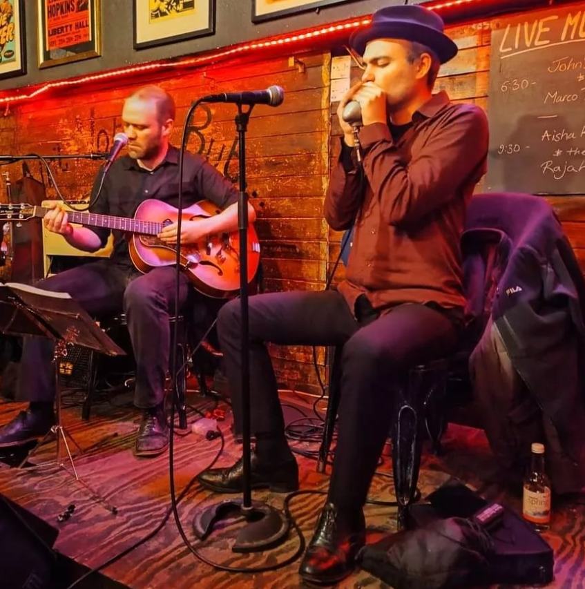 Marco Farris on harmonica in a duo with an archtop guitarist in a blues bar