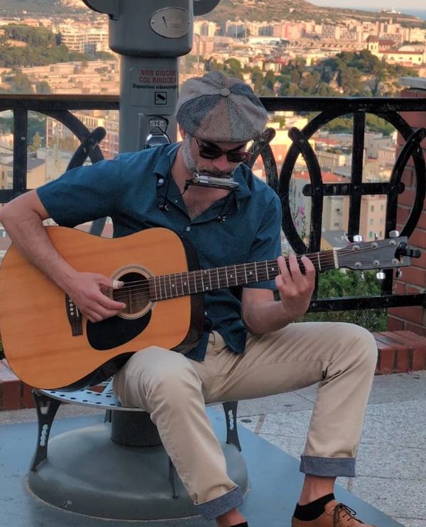 Marco Farris playing acoustic guitar with a harmonica on a neck rack